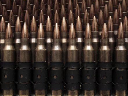 Close-up HD wallpaper of neatly arranged man-made bullets with metallic tips and dark casings, creating a repetitive pattern.