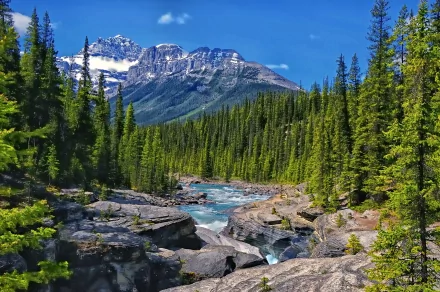 A serene river flows through lush greenery, framed by towering mountains under a clear blue sky. This HD nature scene offers a stunning backdrop for any desktop wallpaper.