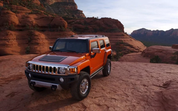 HD PC desktop wallpaper showing an orange Hummer H3 vehicle parked on a rocky desert plateau with red canyon walls and distant mesas beneath a pale sky.