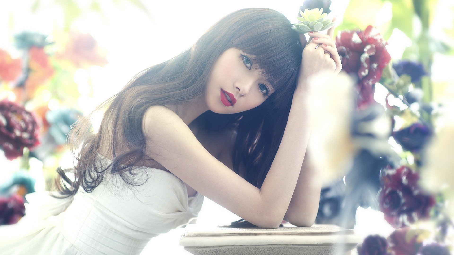 HD desktop wallpaper featuring an Asian woman with long hair in a white dress, leaning on a surface surrounded by vibrant flowers.