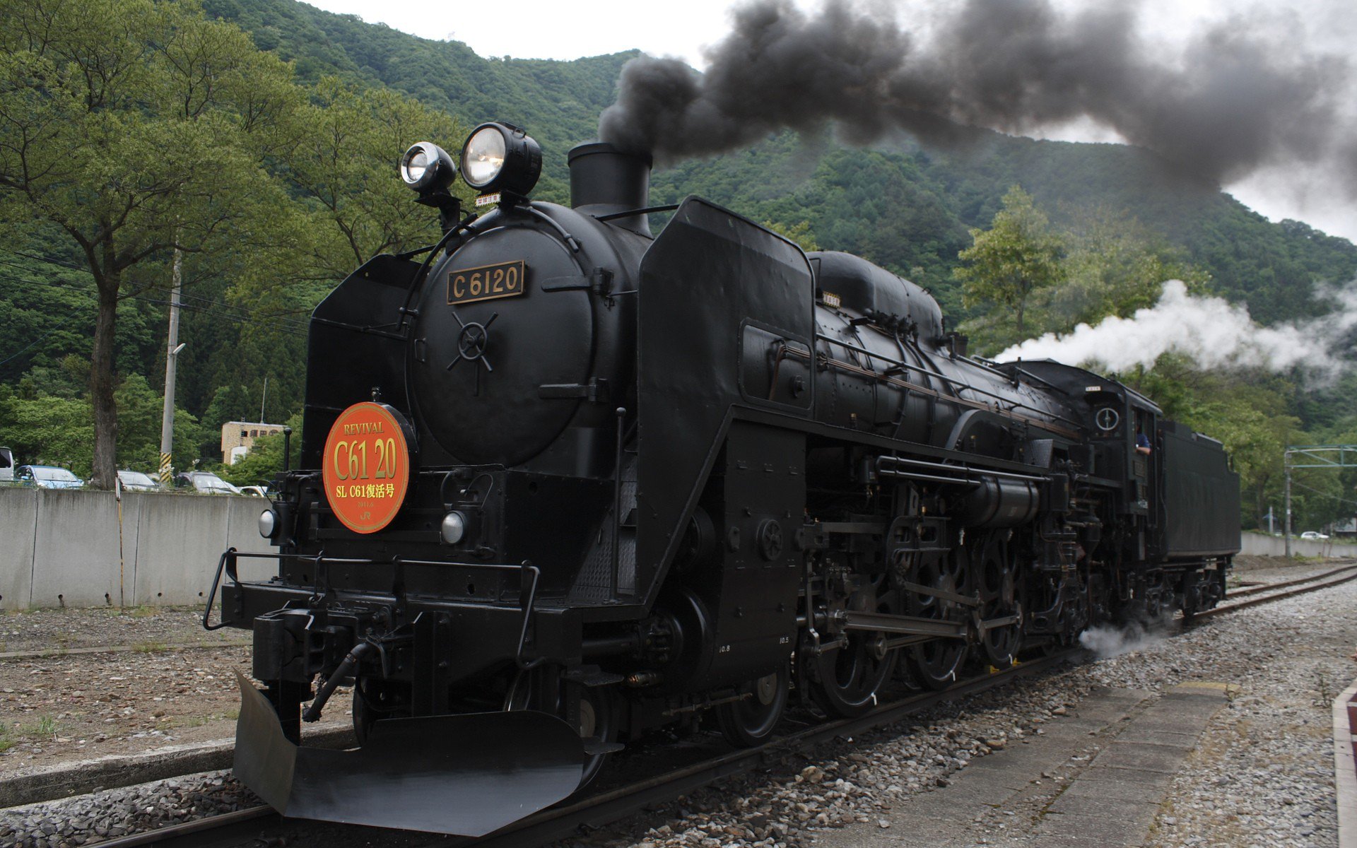 HD PC desktop wallpaper featuring a vintage black steam locomotive emitting smoke as it moves along tracks surrounded by lush green hills.