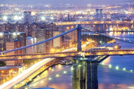 HD PC desktop wallpaper of New York at night: man-made skyline with illuminated bridges spanning the river, vibrant city lights and shimmering reflections.