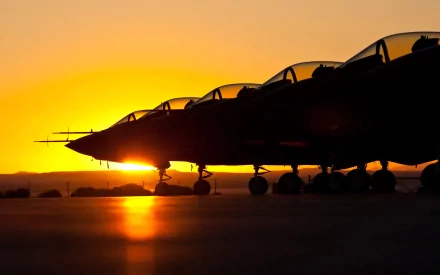 Silhouettes of Lockheed Martin F-35 Lightning II fighter jets lined up on the runway against a vibrant orange sunset, captured in HD for a military-themed desktop wallpaper.