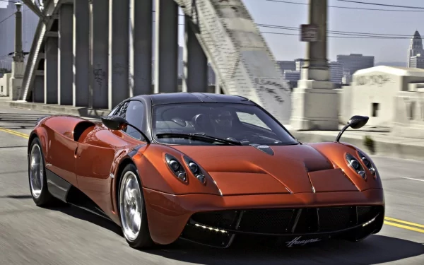 HD desktop wallpaper featuring a sleek red Pagani Huayra driving on a city bridge under clear skies.