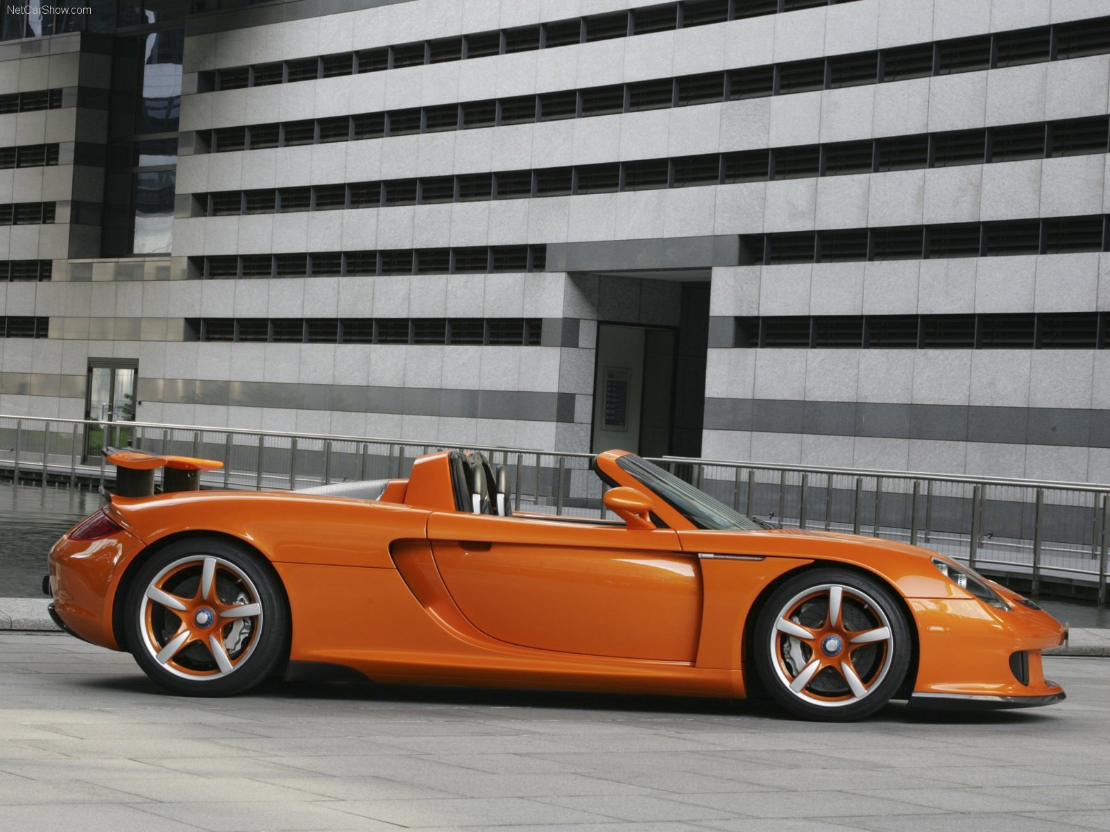 A striking orange Porsche Carrera GT parked in an urban setting, showcasing its sleek design and performance features, serves as a stunning HD desktop wallpaper.