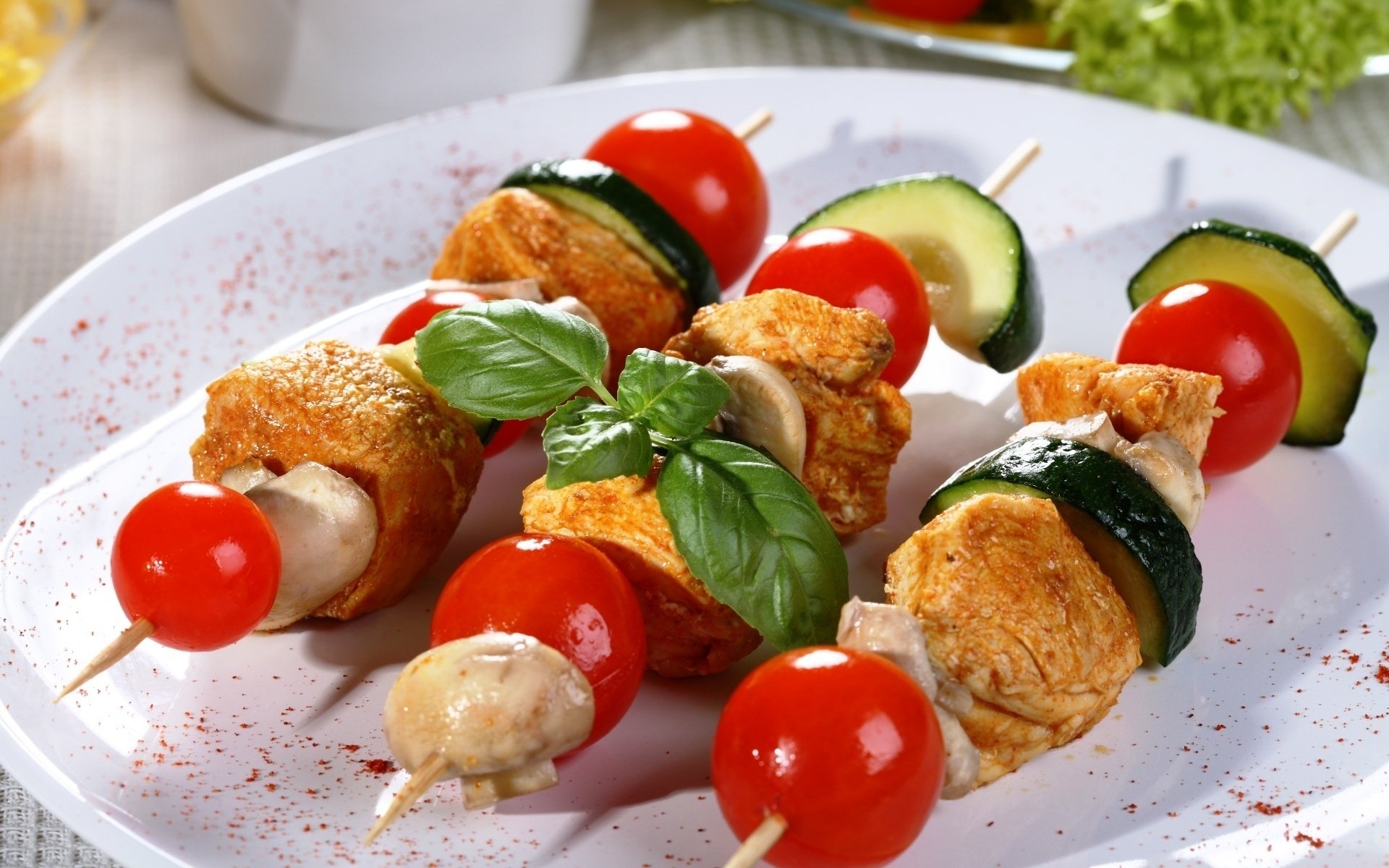 HD PC desktop wallpaper and background of colorful barbecue food skewers — cherry tomatoes, zucchini, mushrooms and seasoned meat on a white plate, garnished with fresh basil.