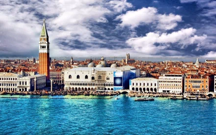 HD desktop wallpaper showcasing the man-made architecture of Venice with historic buildings and a vibrant blue canal under a partly cloudy sky.