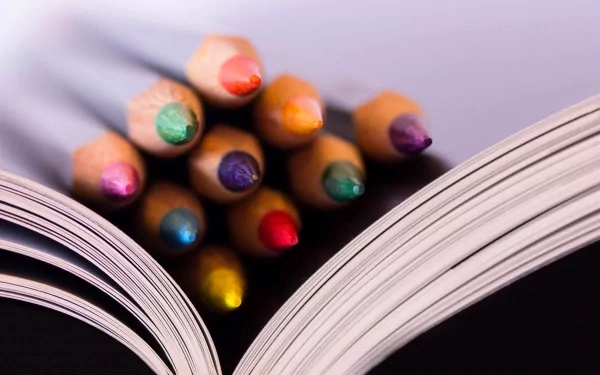HD desktop wallpaper featuring a close-up photograph of colorful pencil tips resting between the pages of an open book.