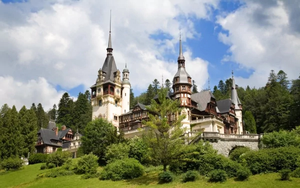 HD desktop wallpaper showcasing the man-made beauty of Peles Castle in Romania, set against a backdrop of lush greenery and a partly cloudy sky.