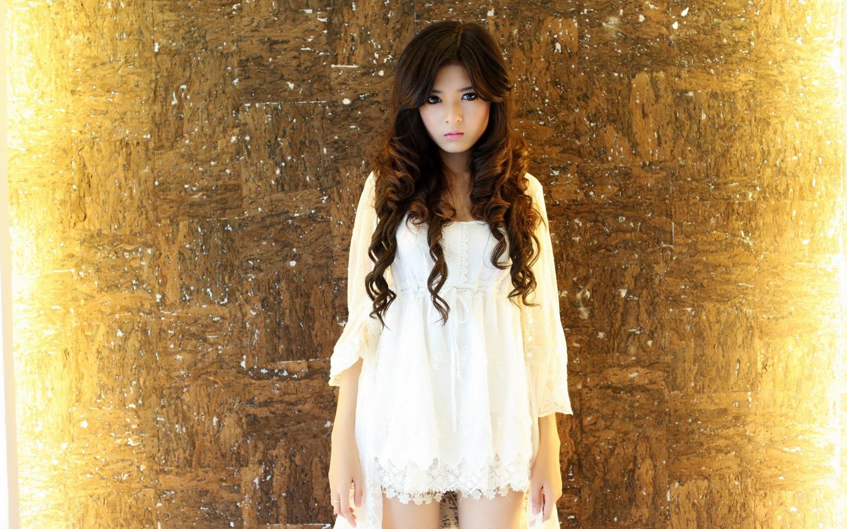 HD desktop wallpaper featuring a model in a white dress standing against a warmly lit, textured background.