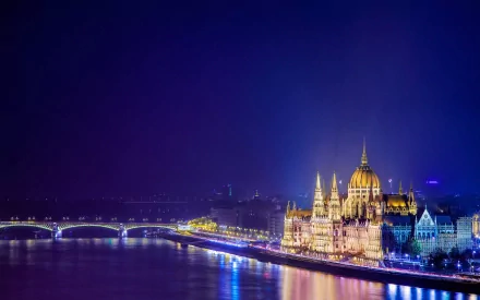 Illuminated Hungarian Parliament Building in Budapest at night, reflecting in the water, showcasing the city's stunning architecture and vibrant colors. A captivating HD desktop wallpaper.