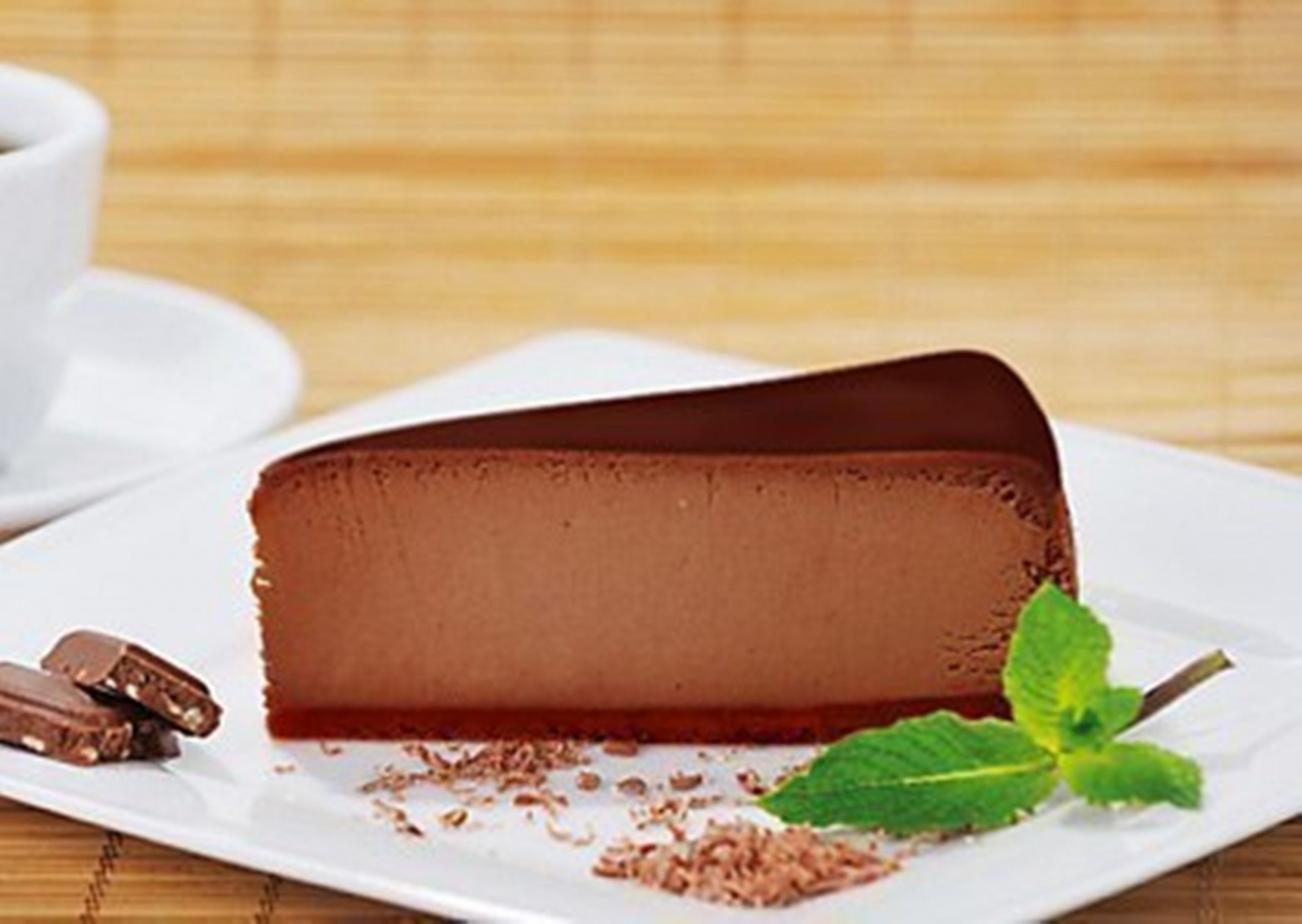 HD desktop wallpaper featuring a rich slice of chocolate cake garnished with mint on a white plate against a wooden background.