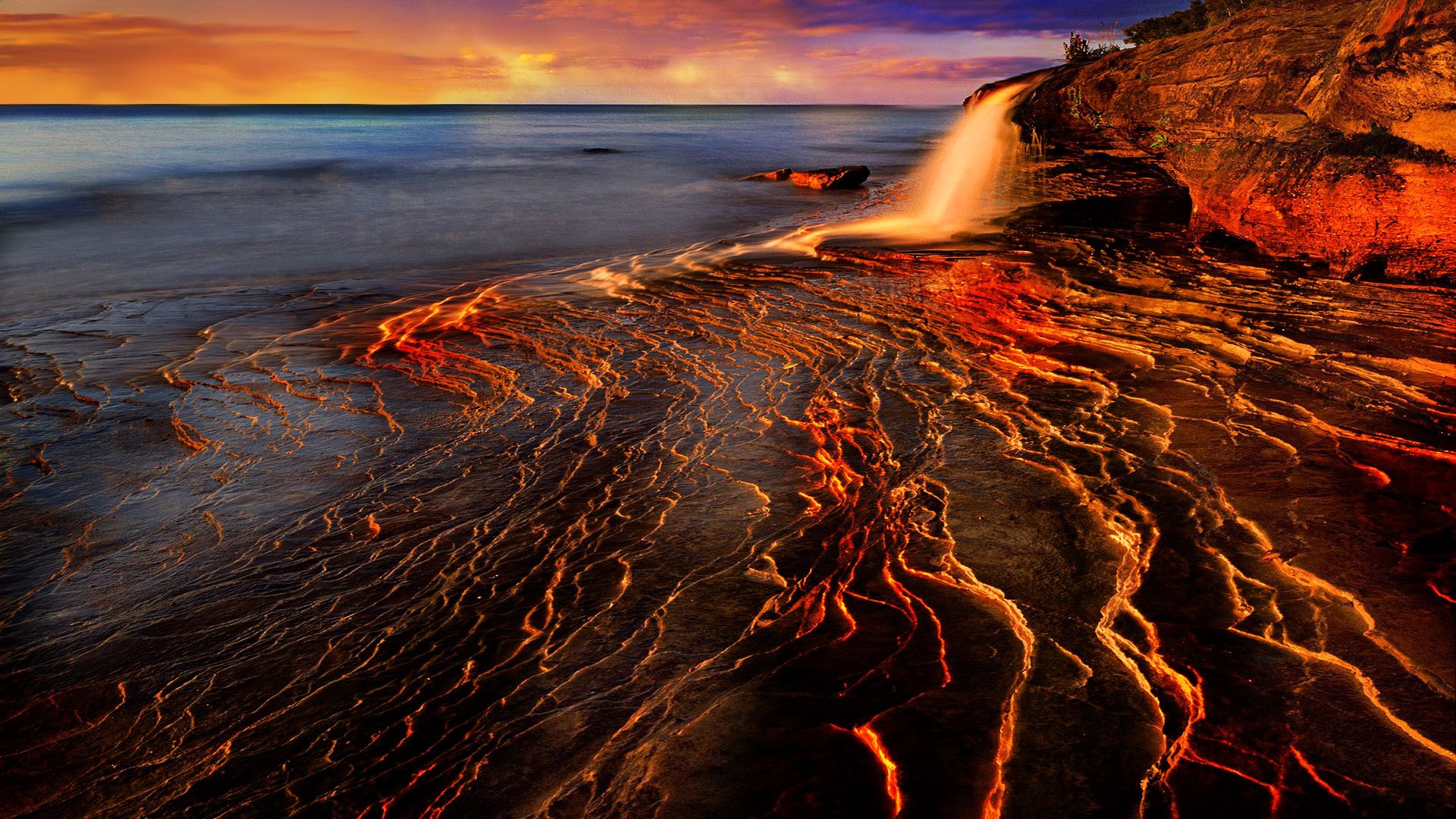 A stunning HD desktop wallpaper featuring a dynamic waterfall cascading over rocky terrain, surrounded by vibrant colors of nature at sunset.