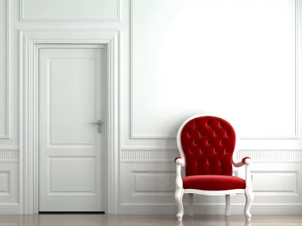 Red upholstered chair against a white paneled wall next to a closed door, featured in a high-definition desktop wallpaper and background.