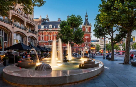 A vibrant scene in Amsterdam showcasing a decorative fountain surrounded by lush trees and historic architecture, capturing the essence of this charming Dutch town.