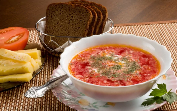 HD PC desktop wallpaper showing a bowl of red soup garnished with herbs, accompanied by sliced bread, cheese, and tomato on a wooden table.