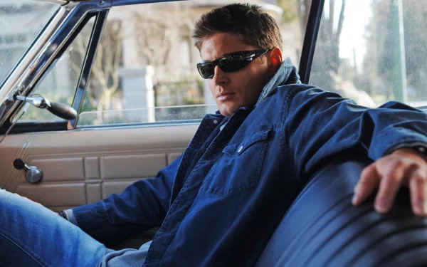 HD desktop wallpaper featuring celebrity Jensen Ackles wearing sunglasses and a denim jacket, seated confidently inside a classic car.