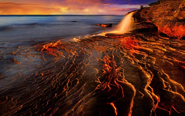 A stunning HD desktop wallpaper featuring a dynamic waterfall cascading over rocky terrain, surrounded by vibrant colors of nature at sunset.