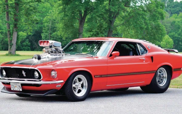 A detailed HD desktop wallpaper featuring a vibrant red 1969 Ford Mustang Mach 1 parked on a road with lush green trees in the background.