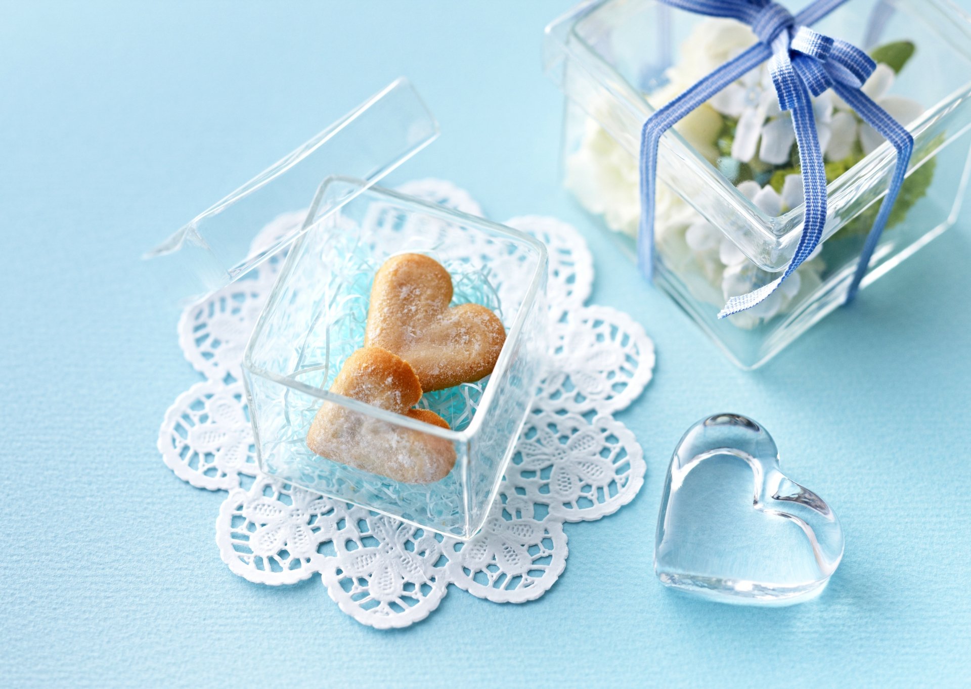 A heart-shaped cookie nestled in a clear box, surrounded by delicate lace and a decorative glass heart, set against a soft blue background, creating an inviting food-themed desktop wallpaper.