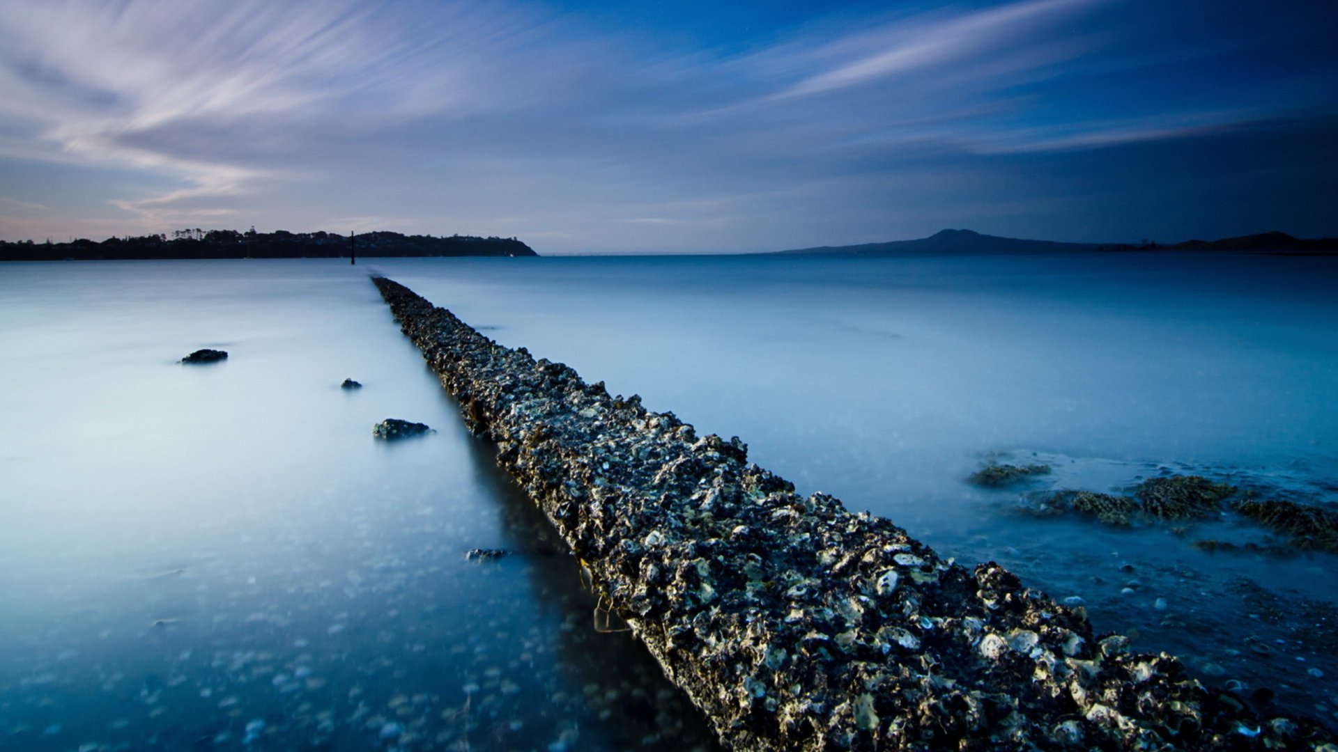 Dusk ocean long-exposure, barnacle-encrusted rock jetty stretching to the horizon; 2K Quad HD PC desktop wallpaper, nature, ocean.