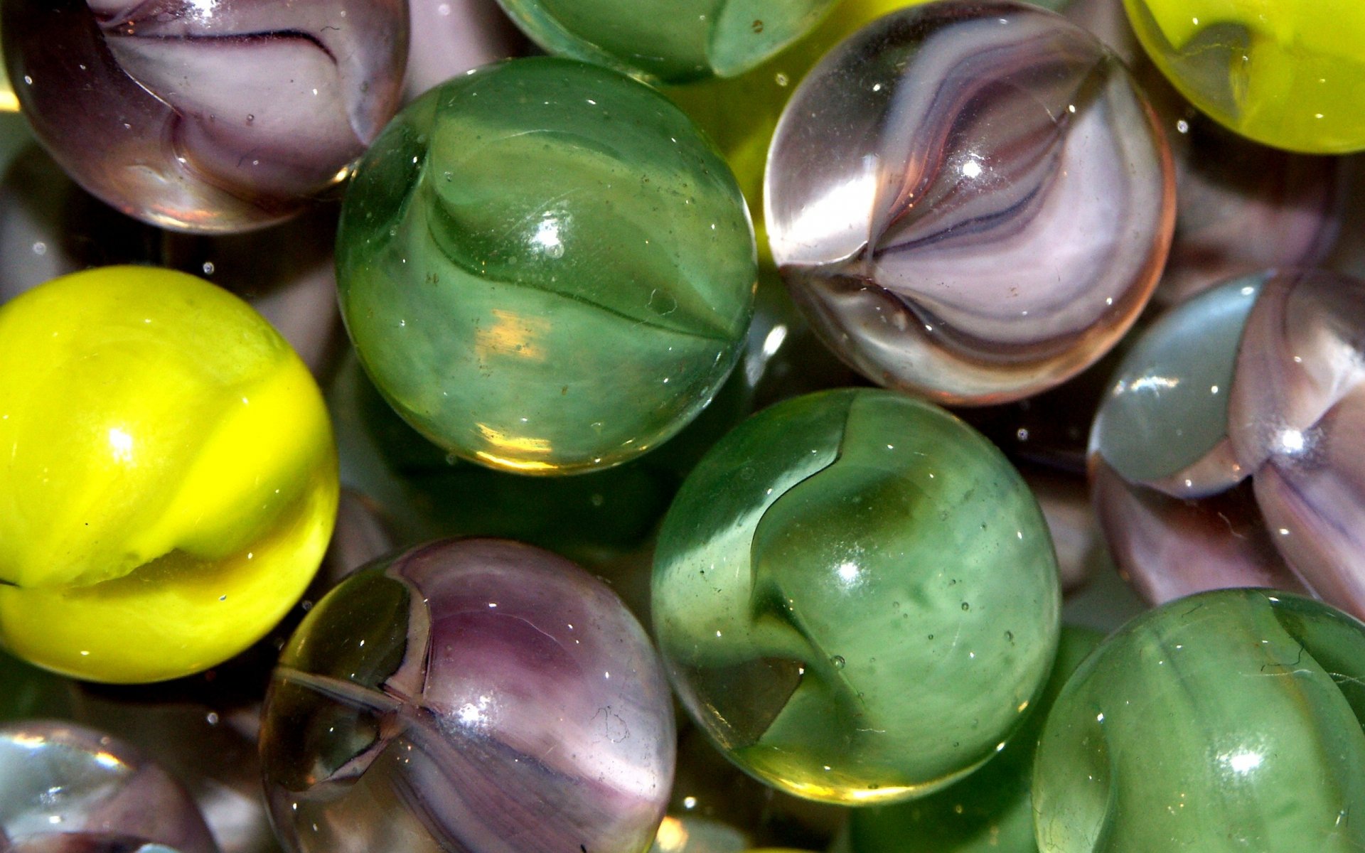 Artistic 3D-rendered marbles with glossy, translucent surfaces in green, purple, and yellow hues, arranged closely in an HD PC desktop wallpaper and background.