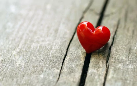 A vibrant red heart rests on a weathered wooden surface, creating an artistic and captivating backdrop for a HD desktop wallpaper.