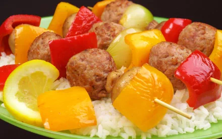 A vibrant dish featuring meatballs and colorful bell peppers arranged on skewers, served over a bed of rice, creating a delightful barbecue-inspired scene in HD.