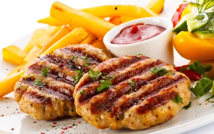 A vibrant HD desktop wallpaper featuring two grilled meat patties topped with herbs, served alongside crispy fries, a side of ketchup, and fresh vegetables on a white plate.