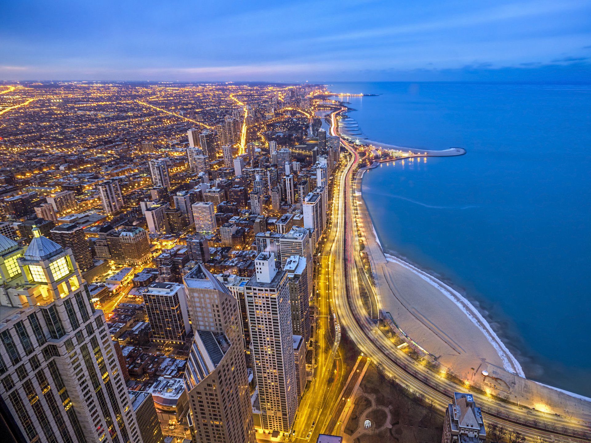 A high-definition desktop wallpaper showing the man-made cityscape of Chicago at dusk, with illuminated streets along the shoreline.