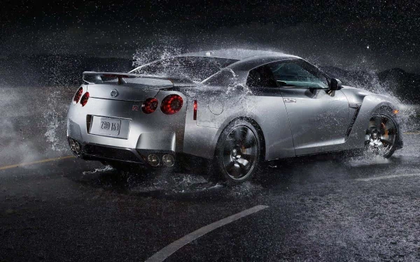 A sleek Nissan GT-R splashes through water on a dark road, captured in a high-definition PC desktop wallpaper showcasing the vehicle's dynamic design.