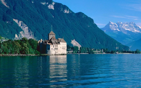 A serene view of Chateau de Chillon, a historic castle on Lake Geneva in Veytaux, Switzerland, surrounded by majestic mountains and clear blue skies.