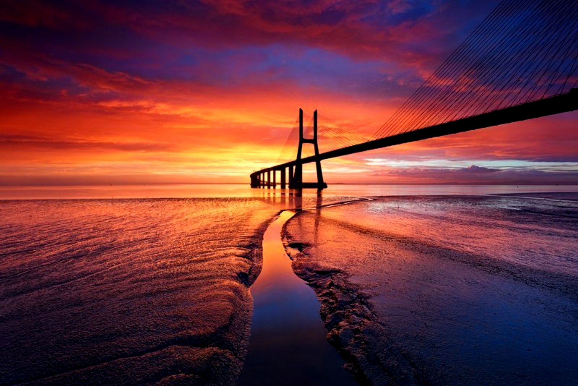 Vibrant sunset over the Vasco da Gama Bridge, a striking man-made structure extending across calm waters in this HD PC desktop wallpaper.