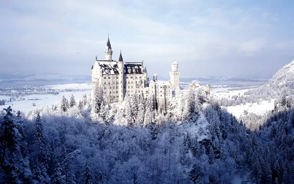 Neuschwanstein Castle stands majestically amidst a snowy landscape, surrounded by frosted trees, making a stunning HD PC desktop wallpaper and background.