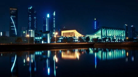 Nighttime skyline of Kuwait City with illuminated modern buildings reflected in calm water, captured as an HD man-made desktop wallpaper background.