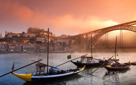 HD desktop wallpaper featuring traditional boats on the Douro River with the iconic Dom Luís I Bridge and Porto cityscape in Portugal at sunrise.