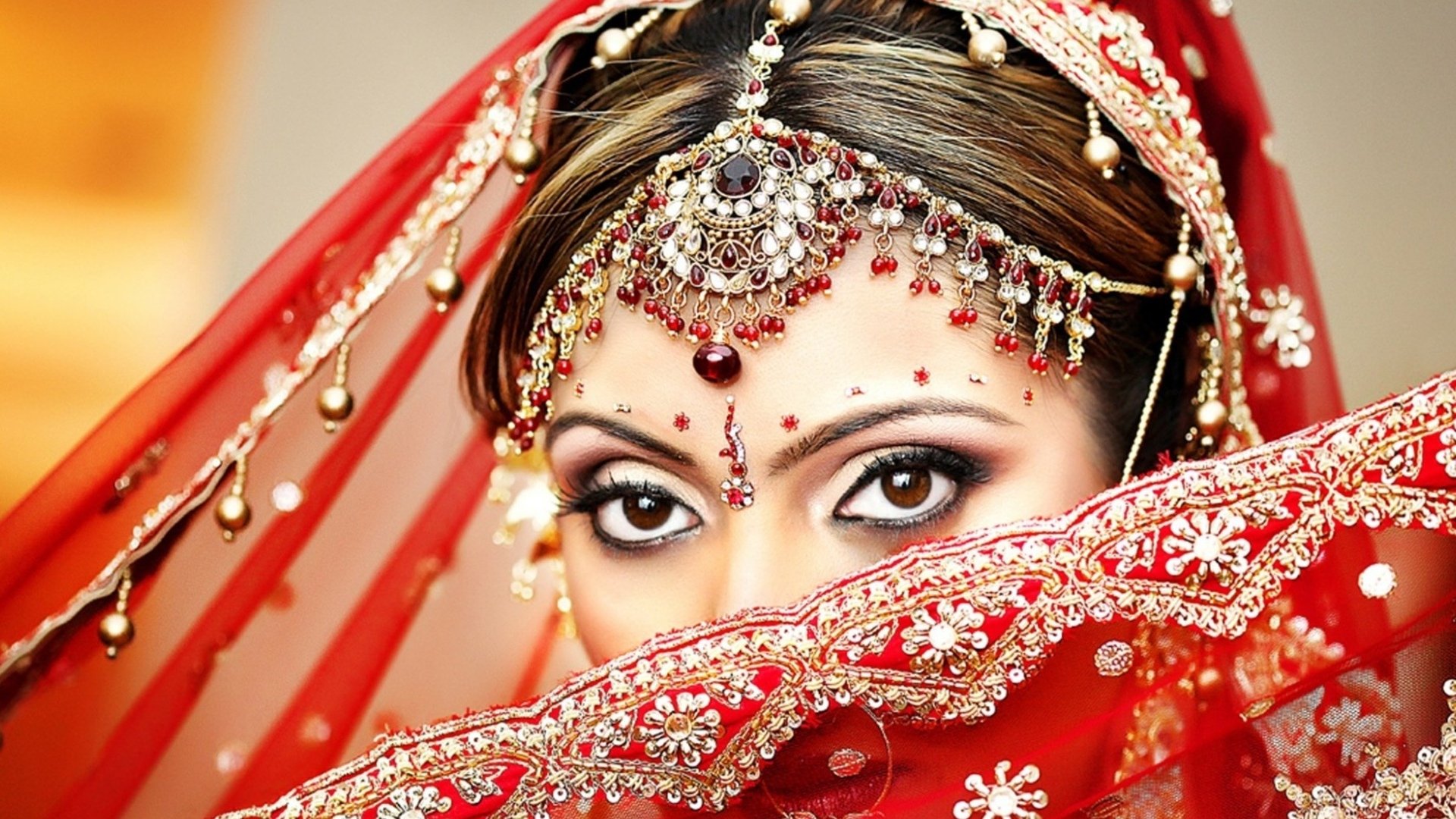 A close-up image of a woman with striking eyes, adorned in elaborate jewelry and a vibrant red veil, serves as an eye-catching HD desktop wallpaper and background.