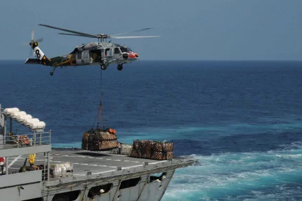 Navy Sikorsky SH-60 Seahawk helicopter airlifting cargo onto a ship at sea, captured in high-definition as a dynamic military vehicle desktop wallpaper.