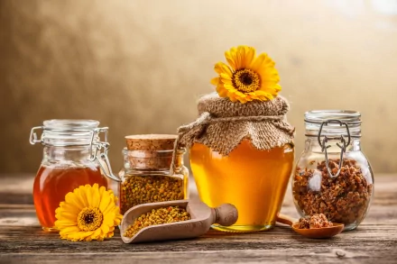 A warm, inviting HD wallpaper featuring jars of honey, bee pollen, and honeycomb, accented with vibrant sunflowers against a soft, golden background.