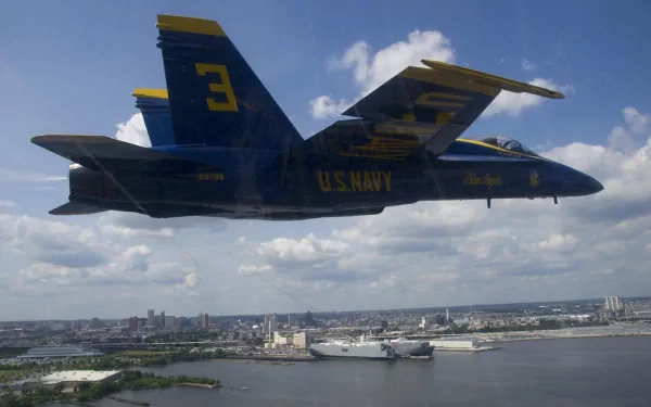 A McDonnell Douglas F/A-18 Hornet from the Blue Angels flies over a coastal cityscape, showcasing the U.S. Navy's military aircraft in crisp HD detail.