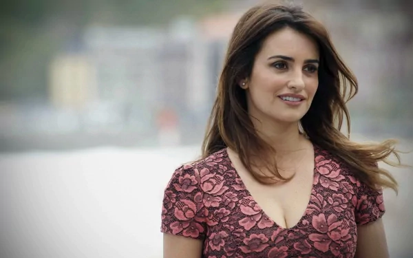 Penelope Cruz smiles warmly in a floral dress, set against a scenic backdrop. This HD image serves as a vibrant desktop wallpaper.