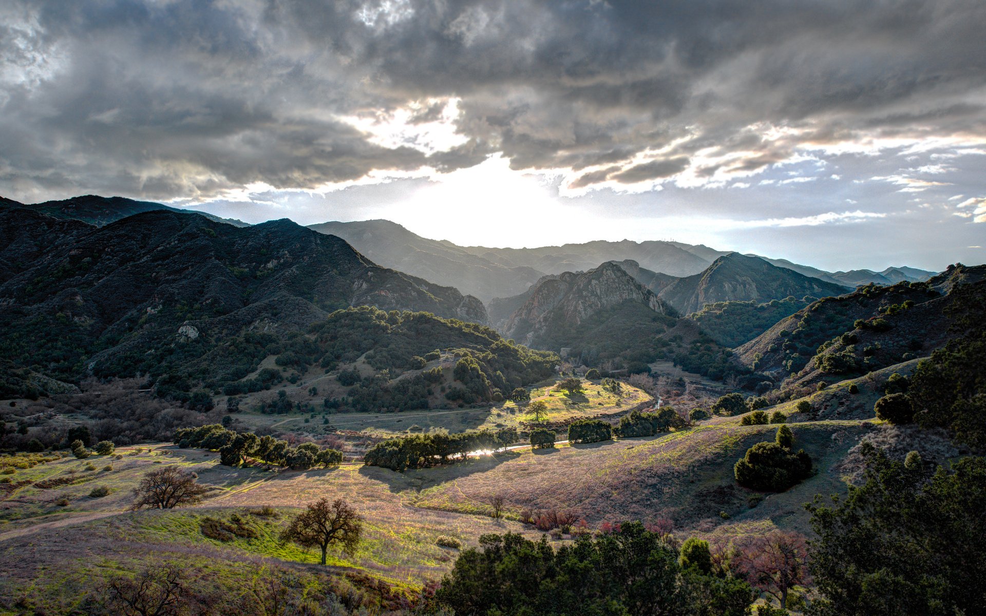 HD desktop wallpaper showcasing a dramatic nature landscape with sun rays breaking through clouds over rolling hills and valleys.