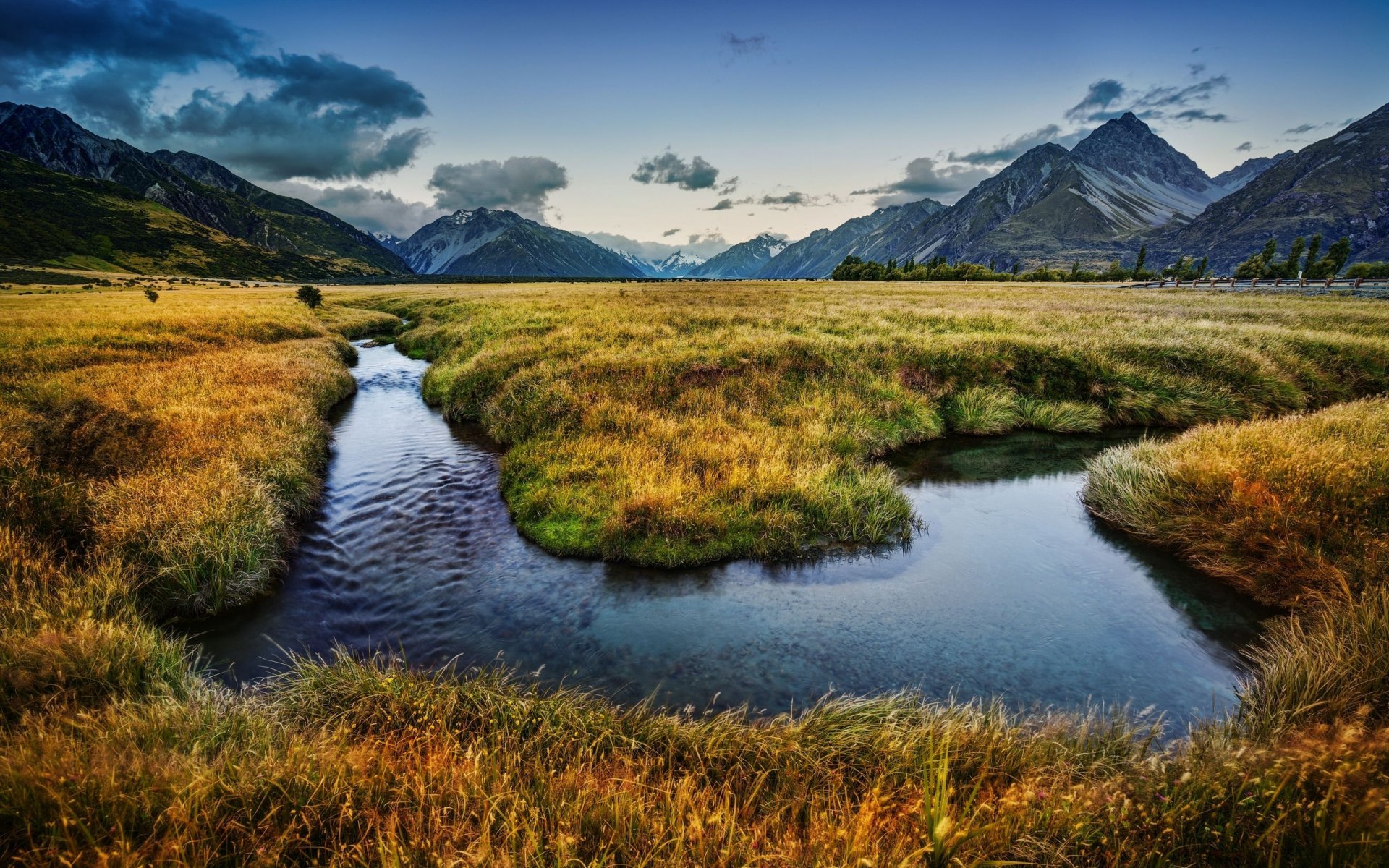 2K Quad HD PC desktop wallpaper: New Zealand meadow with a winding river leading to snow-capped mountains under a dramatic sky, lush nature landscape.