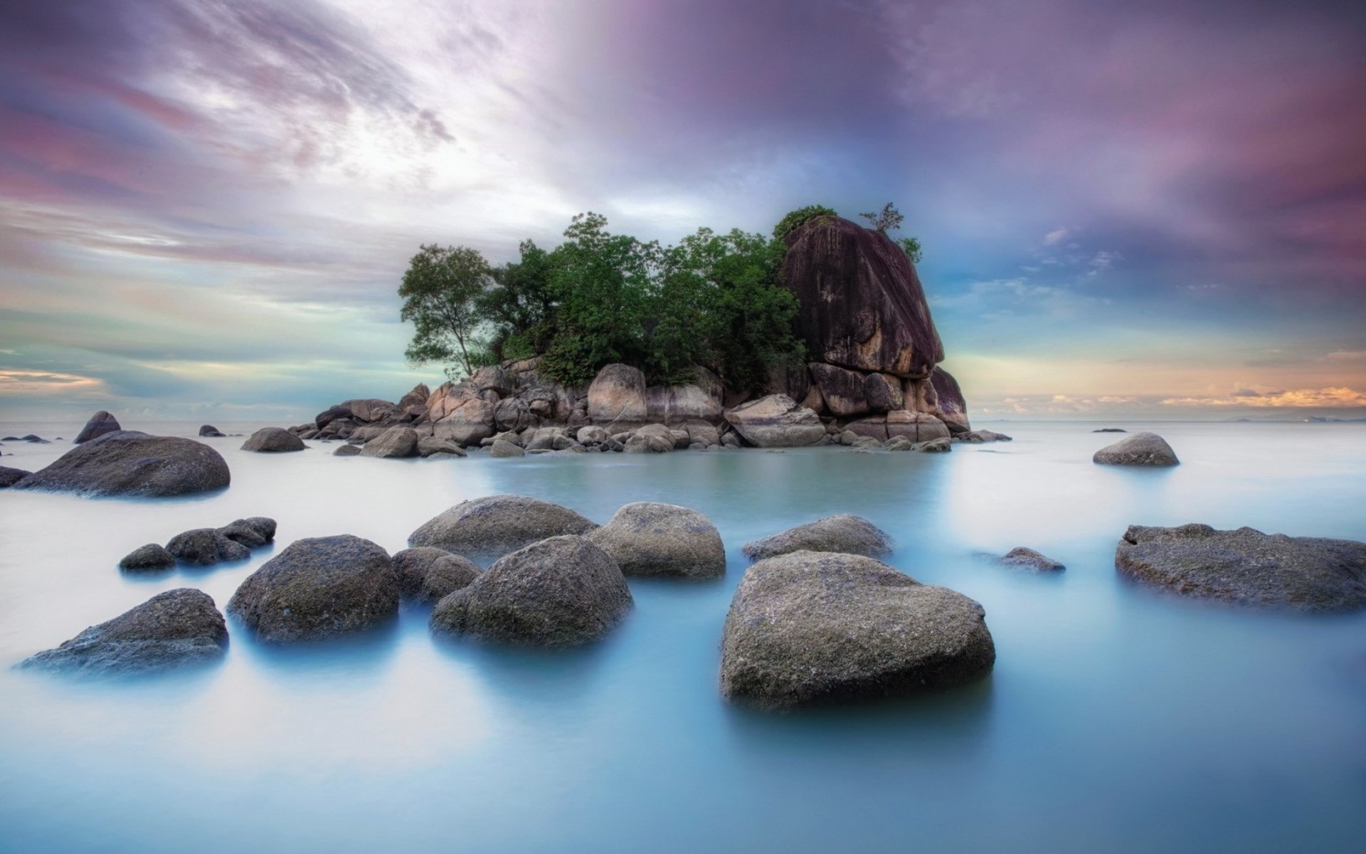 HD PC desktop wallpaper showcasing a serene island surrounded by calm water and scattered rocks under a colorful, cloudy sky, highlighting natural beauty.