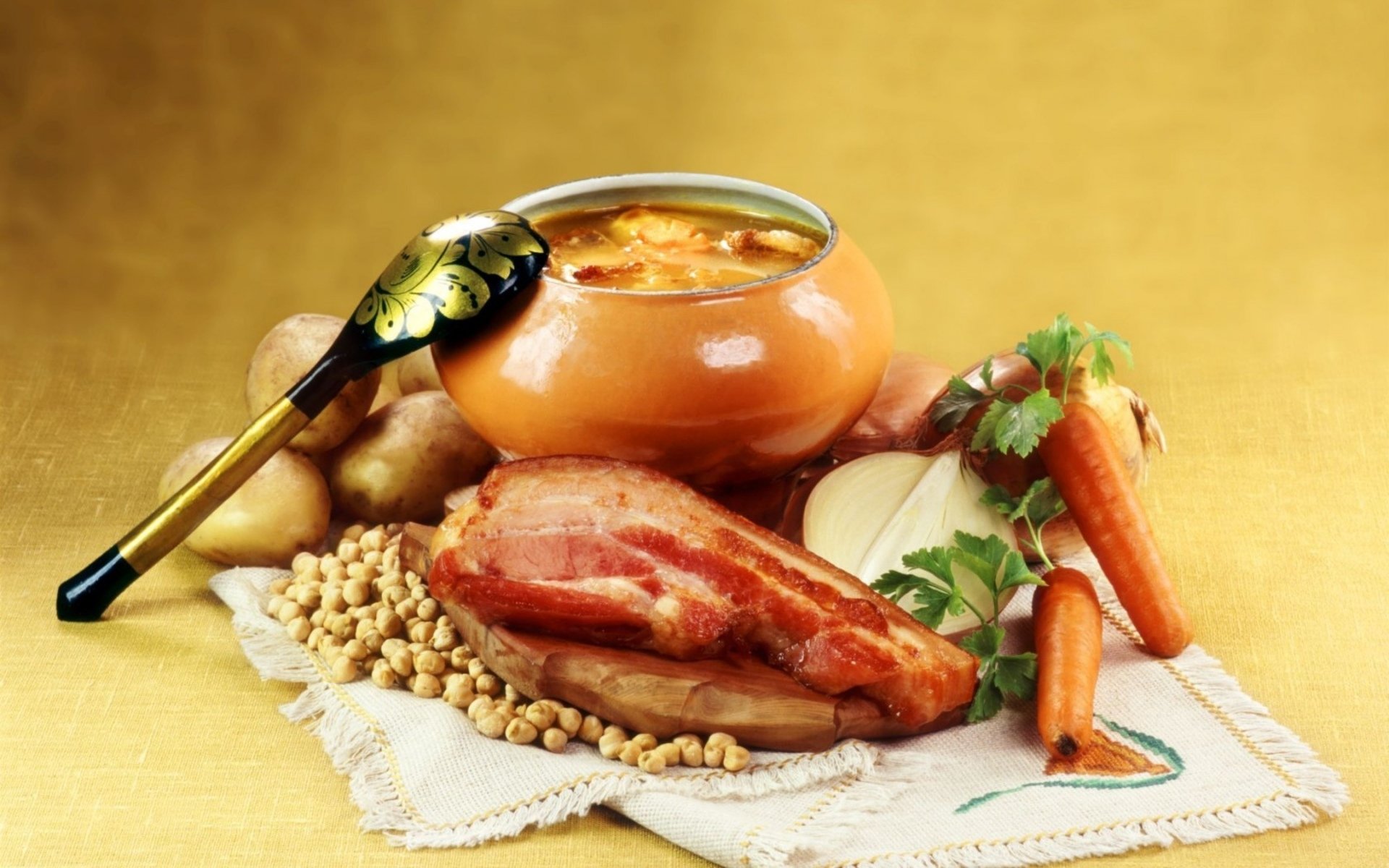 HD PC desktop wallpaper and background showing food: a hearty bowl of soup with ladle, smoked ham, peas, potatoes and carrots on a cloth against a warm golden backdrop.