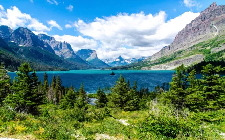 HD desktop wallpaper showing Saint Mary Lake in Glacier National Park with mountains, a clear blue lake, and lush greenery under a vibrant blue sky with clouds.
