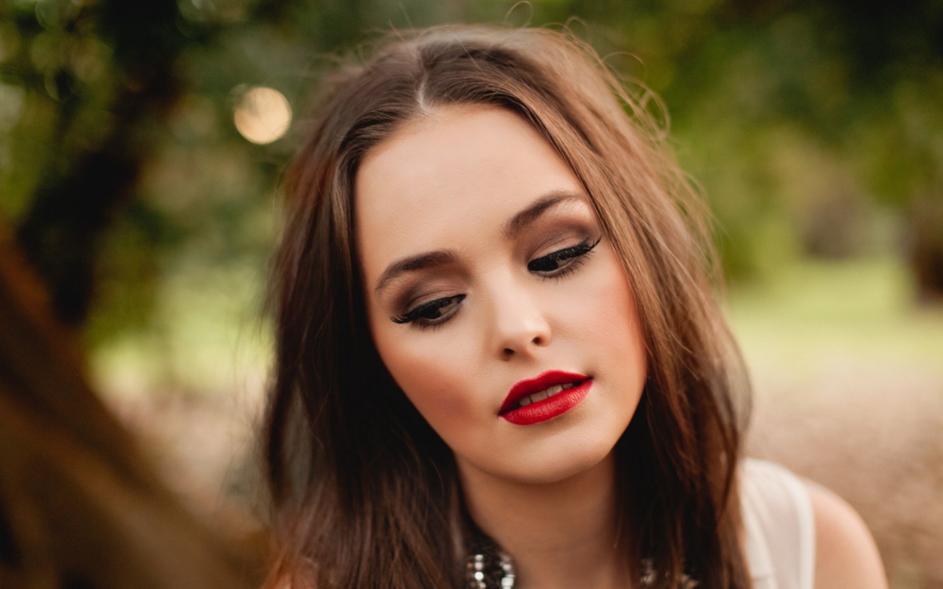 HD desktop wallpaper of a woman with long brown hair, red lipstick, and soft makeup, set against a blurred natural background.