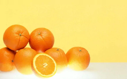 HD desktop wallpaper featuring a group of vibrant oranges against a soft yellow background, highlighting fresh food with bright orange tones.