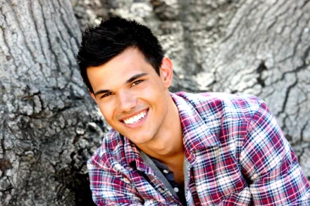 A high-definition desktop wallpaper featuring celebrity Taylor Lautner smiling confidently, framed by the texture of a tree trunk in a casual plaid shirt.