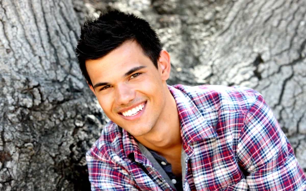 A high-definition desktop wallpaper featuring celebrity Taylor Lautner smiling confidently, framed by the texture of a tree trunk in a casual plaid shirt.